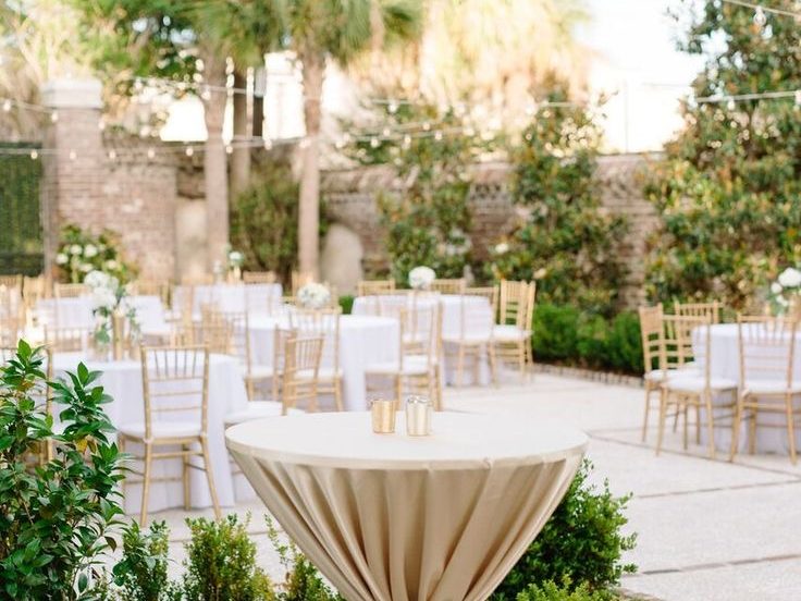 Mesa alta de cóctel con mantel en un jardín preparado para el evento